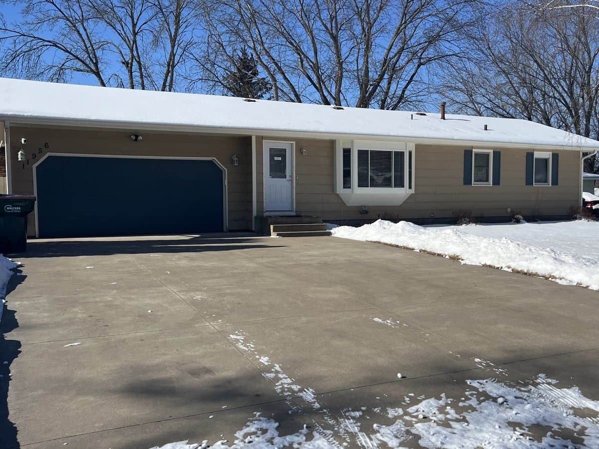Tan single-story residential assisted living home with a navy two-car garage door and wide driveway in winter in Blaine, MN