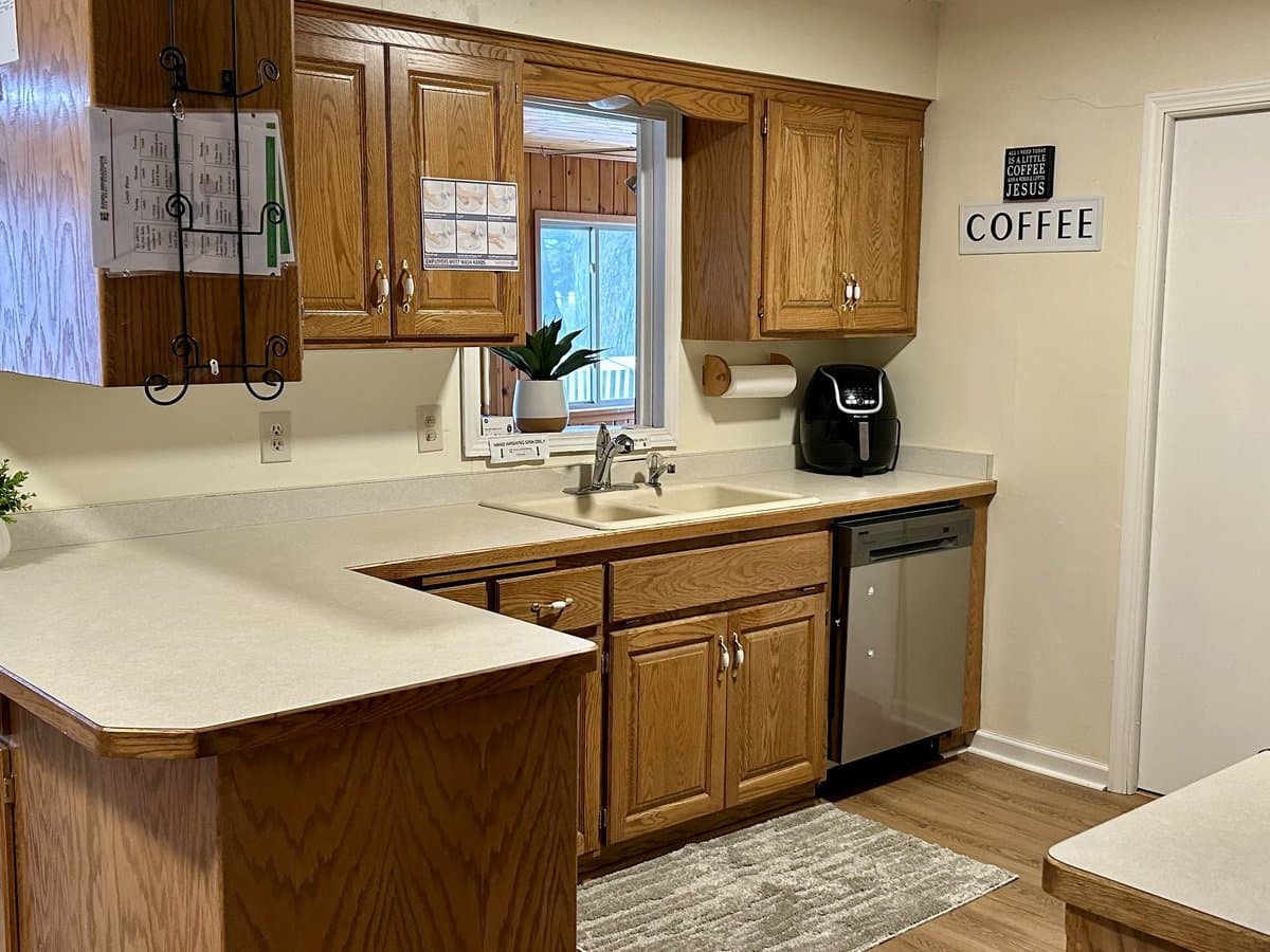Kitchen with oak cabinets, a corner counter, stainless dishwasher, and a window over the sink