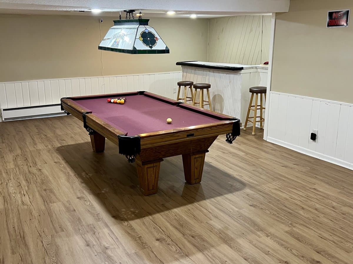 Lower-level living room with a pool table, bar seating, and wood-look flooring