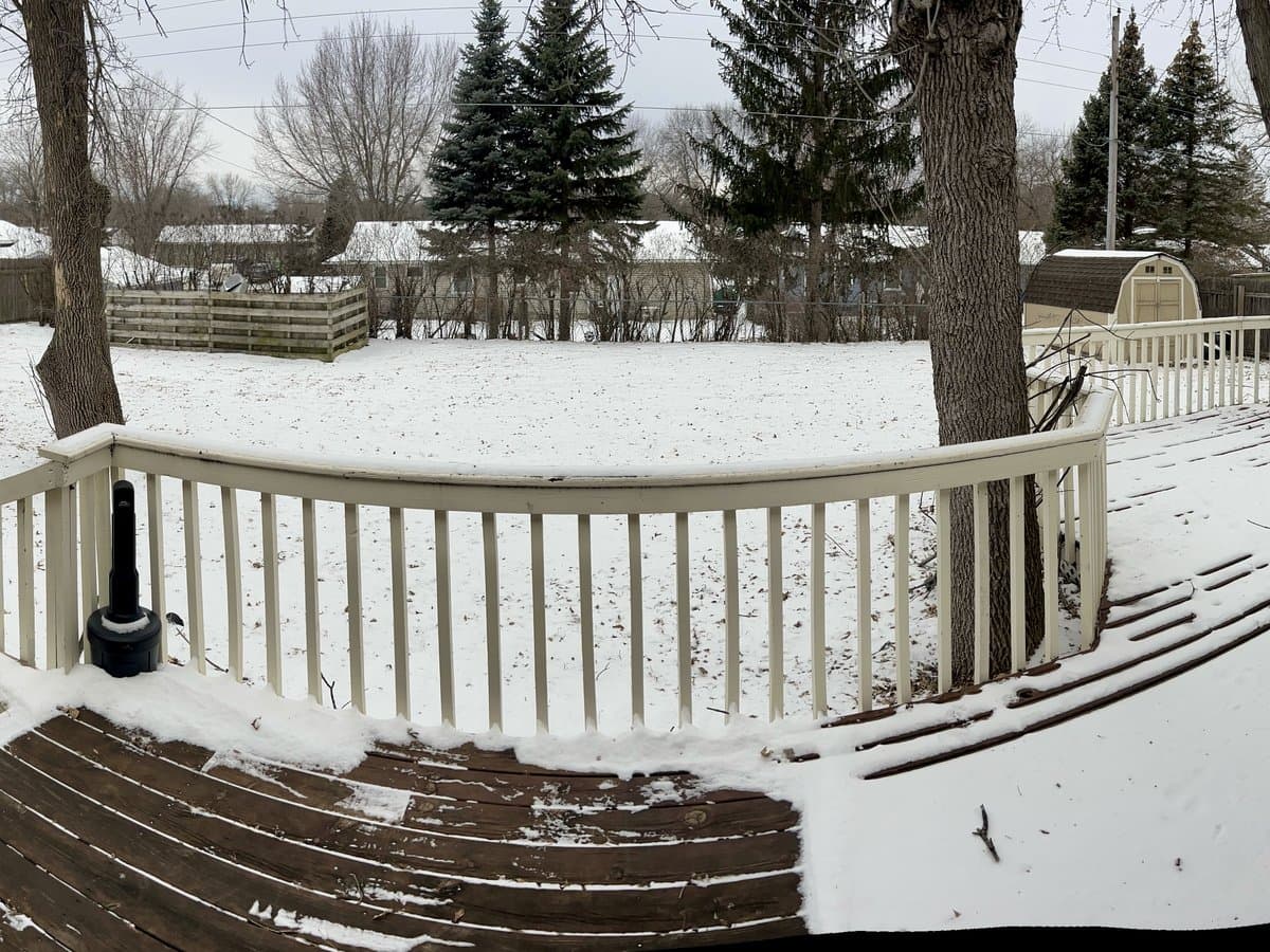 Back deck with white railings overlooking a large snow-covered fenced yard