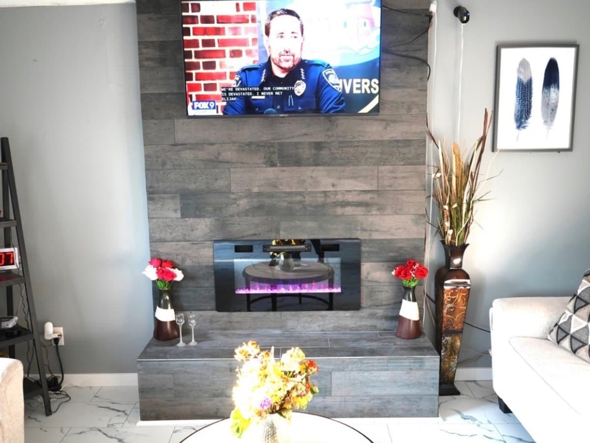 Living room with a tiled electric fireplace wall, mounted TV, and white sofas in a Maple Grove, MN residential assisted living home