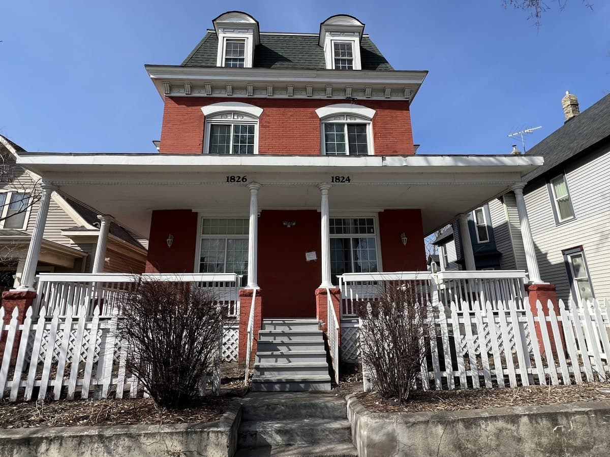 Historic red-brick home with a covered porch and white picket fence in Minneapolis, MN